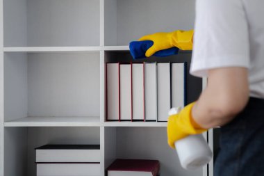 Odayı temizleyen kişi, temizlik personeli şirket ofisindeki kitaplığı silmek için bez ve dezenfektan kullanıyor. Temizlik personeli. Organizasyondaki temizliği sürdürmek.