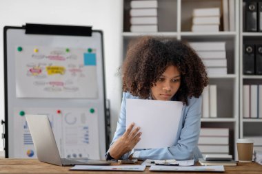 Girişimci bir şirkette çalışan Amerikalı bir kadın, ofiste çalışan Amerikalı bir iş kadını, yöneticilerle görüşmeden önce finansal belgelere ve satış verilerine bakıyor..