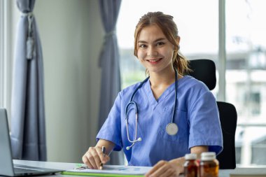 Tıbbi giysiler içinde genç ve güzel bir bayan doktor bir hastane ofisinde oturur ve çalışır, profesyonel bir doktor ve bir hastaya danışır, bir hastalığı detaylı bir şekilde tedavi eder. Kadın doktor konsepti.