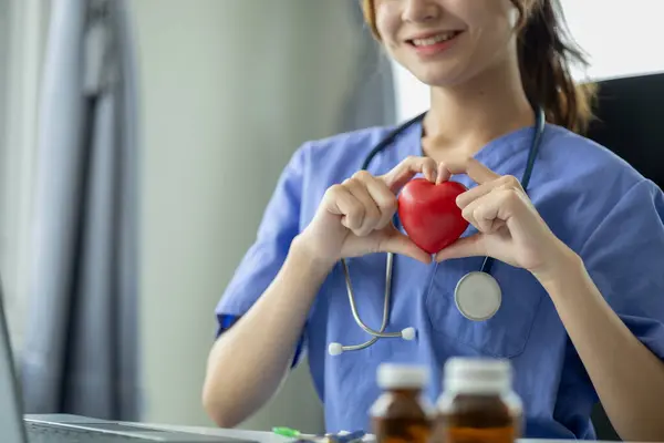 Beautiful young woman doctor in medical uniform holding a small fake heart, medical professional and consultation, treatment, cardiologist. Concept of female doctor in cardiology.