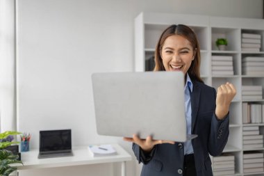 Şirketin kârlı satışlarına ve kazanç özetine bakan Asyalı kadın, mutlu bir ifade sergiliyor, şirketin hedefine ulaşmasından ve daha fazla büyümesinden memnun..