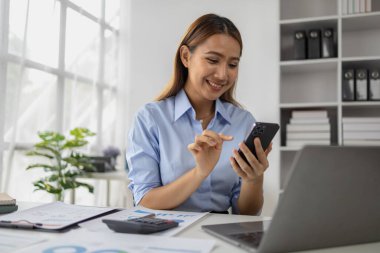 Asyalı bir kadın cep telefonuyla şirket ofisindeki bilgilerini yazıyor, iş kadını üst düzey yönetici şirketi akıllı telefon kullanıyor, iş görüşmeleri yapıyor. İş yönetimi kavramı.