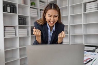 Şirketin kârlı satışlarına ve kazanç özetine bakan Asyalı kadın, mutlu bir ifade sergiliyor, şirketin hedefine ulaşmasından ve daha fazla büyümesinden memnun..