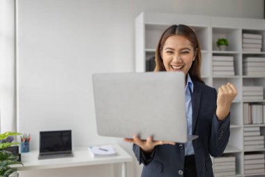 Şirketin kârlı satışlarına ve kazanç özetine bakan Asyalı kadın, mutlu bir ifade sergiliyor, şirketin hedefine ulaşmasından ve daha fazla büyümesinden memnun..