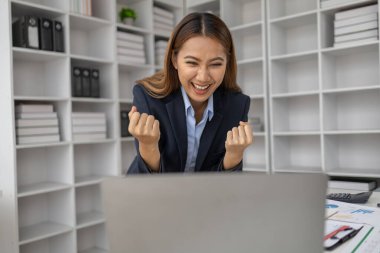 Şirketin kârlı satışlarına ve kazanç özetine bakan Asyalı kadın, mutlu bir ifade sergiliyor, şirketin hedefine ulaşmasından ve daha fazla büyümesinden memnun..