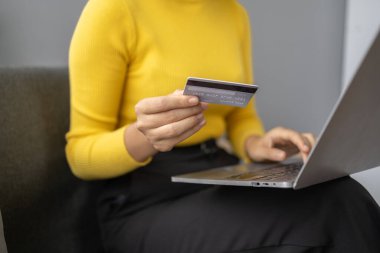 Asyalı bir kadın oturma odasında dinleniyor, iş kadını tatilini internet sitesinde alışveriş yaparak geçiriyor, web sitesinden alışveriş yapıyor ve kredi kartıyla ödüyor. İnternet üzerinden ödeme yapmak için kredi kartı kullanma kavramı.