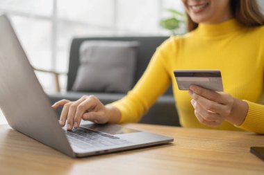 Asyalı bir kadın oturma odasında dinleniyor, iş kadını tatilini internet sitesinde alışveriş yaparak geçiriyor, web sitesinden alışveriş yapıyor ve kredi kartıyla ödüyor. İnternet üzerinden ödeme yapmak için kredi kartı kullanma kavramı.