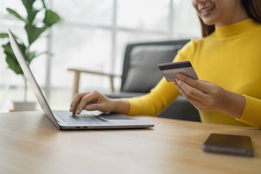 Asyalı bir kadın oturma odasında dinleniyor, iş kadını tatilini internet sitesinde alışveriş yaparak geçiriyor, web sitesinden alışveriş yapıyor ve kredi kartıyla ödüyor. İnternet üzerinden ödeme yapmak için kredi kartı kullanma kavramı.