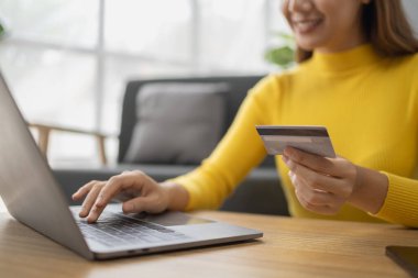 Asyalı bir kadın oturma odasında dinleniyor, iş kadını tatilini internet sitesinde alışveriş yaparak geçiriyor, web sitesinden alışveriş yapıyor ve kredi kartıyla ödüyor. İnternet üzerinden ödeme yapmak için kredi kartı kullanma kavramı.