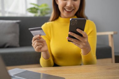 Asyalı bir kadın oturma odasında dinleniyor, iş kadını tatilini internet sitesinde alışveriş yaparak geçiriyor, web sitesinden alışveriş yapıyor ve kredi kartıyla ödüyor. İnternet üzerinden ödeme yapmak için kredi kartı kullanma kavramı.