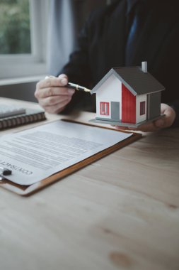 Emlakçı müşteriye bir örnek ev modeli sunuyor, emlakçı evin detaylarını ve satışın sözleşme şartlarını açıklıyor. Konut satma kavramı.