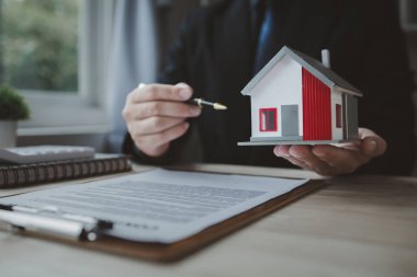 Emlakçı müşteriye bir örnek ev modeli sunuyor, emlakçı evin detaylarını ve satışın sözleşme şartlarını açıklıyor. Konut satma kavramı.
