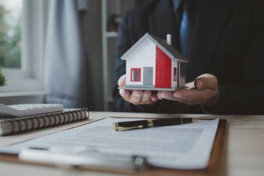Emlakçı müşteriye bir örnek ev modeli sunuyor, emlakçı evin detaylarını ve satışın sözleşme şartlarını açıklıyor. Konut satma kavramı.