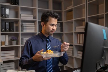 Bir şirket çalışanı işten sonra fazla mesai yapar, gecenin bir yarısı ofisinin masasında bilgisayarın önünde akşam yemeği yer. Fazla mesai ve sıkı çalışma konsepti.
