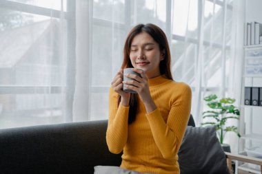 Oturma odasında kanepede oturan Asyalı kadın, tatilde olan kadın ofis çalışanı, tatilde ve boş zamanlarında evde olan, hafta sonu tatilinde evde aile aktiviteleri yapan..