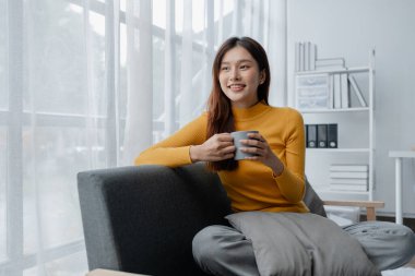 Oturma odasında kanepede oturan Asyalı kadın, tatilde olan kadın ofis çalışanı, tatilde ve boş zamanlarında evde olan, hafta sonu tatilinde evde aile aktiviteleri yapan..