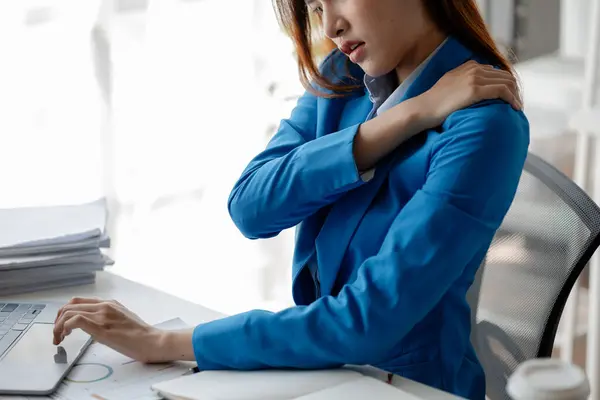 Asian woman in a startup company office, businesswoman poses stressed and body aches due to long hours of hard work, office syndrome among working people. Office syndrome concept and hard work.