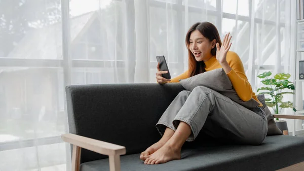 Asian woman in living room and video call with friend on smartphone, female company worker with vacation, spending vacation and leisure time at home, weekend vacation doing activities.