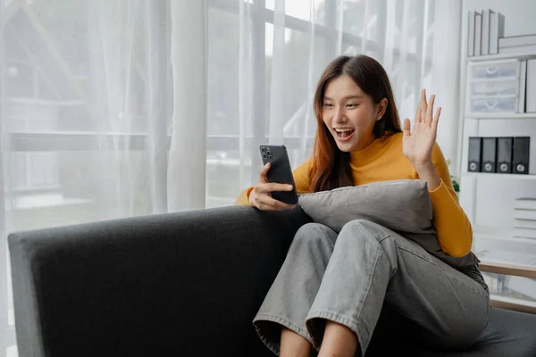 Asian woman in living room and video call with friend on smartphone, female company worker with vacation, spending vacation and leisure time at home, weekend vacation doing activities.