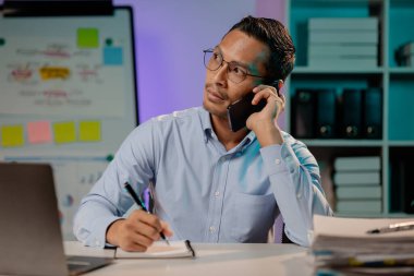 Yeni başlayan bir şirketin ofisinde Asyalı bir adam telefonda konuşuyor. Fazla mesai yapan şirket çalışanları, gece mesaisi, yoğun ve çalışkan bir şirket çalışanının fazla mesaisi. Fazla mesai kavramı.