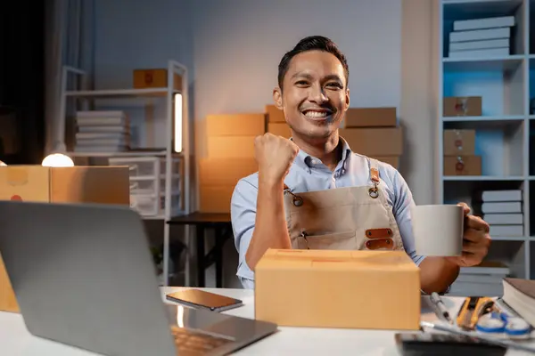Business owner sells products on websites and online platforms. He has a happy expression. Business owner sells products and packs the products in boxes to deliver to the customer via courier service.