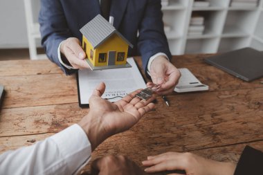 Projede gayrimenkul ve ev satışları düzenleniyor. Birkaç kez gidip bir satıcıyla ev almayı tartışmışlar. Konut projesi satıcısı ev alıp satmanın detaylarını açıklıyor.