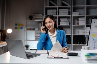 İş kadını, yeni başlayan bir şirketin ofisinde telefonla konuşuyor. Pazarlama personeli satışları artırmak için pazarlama planları yapıyor. Telefon görüşmelerinde iletişim kuruyor. Pazarlama yönetimi kavramları.