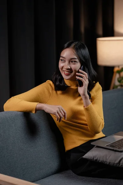 Asian woman relaxing on sofa in house, businesswoman spends her vacation watching movies, listening to music and surfing social media on smartphone, texting and chatting with friends. Weekend concept.