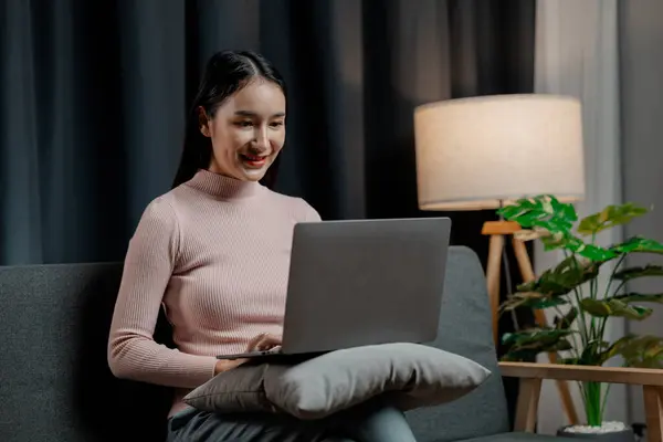Asian woman in the living room with laptop, female company employee on vacation, using vacation time and free time to relax at home, weekend vacation doing activities.