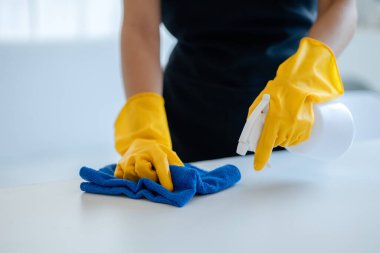 Ofisteki masa yüzeyini dezenfektan spreyiyle temizlemek, eldiven giymek ve masayı havluyla silmek, temizlikçi, temizlik için çalışma masasını temizliyor çünkü Covid-19, temizlik fikri....