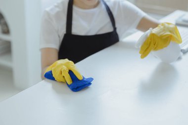 Ofisteki masa yüzeyini dezenfektan spreyiyle temizlemek, eldiven giymek ve masayı havluyla silmek, temizlikçi, temizlik için çalışma masasını temizliyor çünkü Covid-19, temizlik fikri....