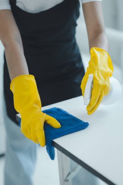 Ofisteki masa yüzeyini dezenfektan spreyiyle temizlemek, eldiven giymek ve masayı havluyla silmek, temizlikçi, temizlik için çalışma masasını temizliyor çünkü Covid-19, temizlik fikri....