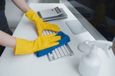 Ofis ekipmanlarını temizleyen, klavyeyi bir havlu ve dezenfektanla temizleyen. Temizlik kimyasallarıyla çalışırken lastik eldiven tak, temizlik fikri....