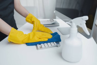 Ofis ekipmanlarını temizleyen, klavyeyi bir havlu ve dezenfektanla temizleyen. Temizlik kimyasallarıyla çalışırken lastik eldiven tak, temizlik fikri....