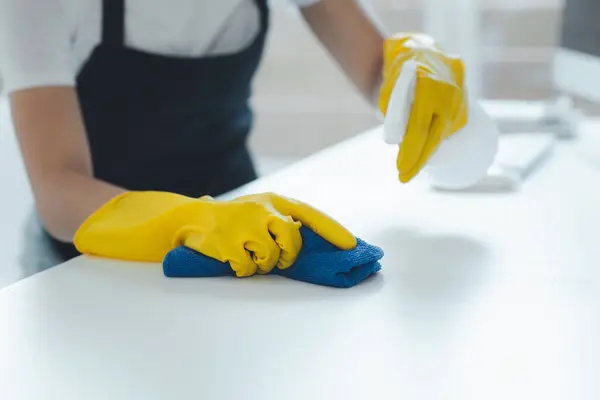 Cleaning desk surface in office with sanitizer spray, wear gloves and wipe the table with a towel, the housekeeper is cleaning the work desk for hygiene because of the Covid-19, cleaning idea.