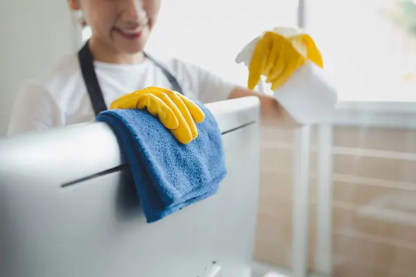 Asian female cleaner, Wear rubber gloves and an apron and work with a happy smile, Cleaning staff wiping down office equipment, Wipe the monitor clean with a towel and sanitizer, cleaning idea.