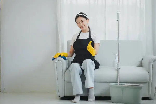The cleaning staff is cleaning the furniture inside the house, Wear rubber gloves and an apron and work with a happy smile, Use a towel to wipe the couch, cleaning idea.