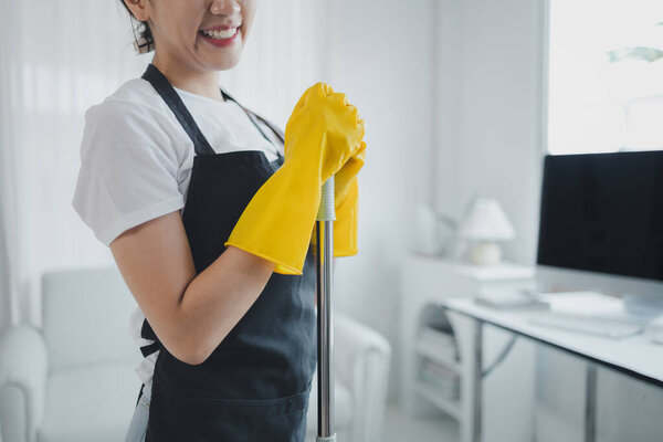 Азиатские женщины носят униформу, чтобы подготовиться к работе по дому, носить фартук и резиновые перчатки, чтобы защитить от чистки химических веществ, экономка улыбается счастливо, прежде чем начать работу, уборка идея