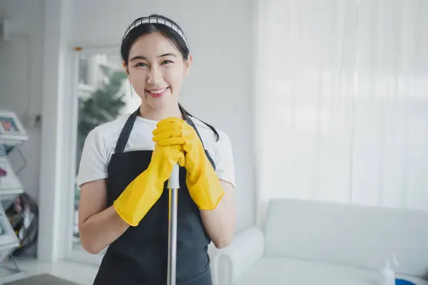 Asian women wear uniforms to prepare for housekeeping work, Wear an apron and rubber gloves to protect against cleaning chemicals, housekeeper is smiling happily before starting work, cleaning idea