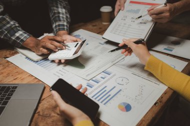 Gelirleri hesaplamak için birlikte çalışan bir grup işadamı, finansal rakamları gözden geçiriyorlar, finansal belgeleri çıkarıyorlar ve onları bir hesap makinesiyle, finansal fikirle kontrol ediyorlar..