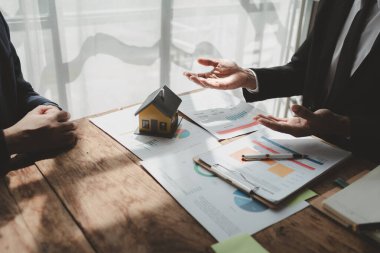 Bir emlak uzmanıyla, emlak yatırımlarıyla ilgili görüşmeler yapan bir müşteri, bir yatırım uzmanıyla gayrimenkul satın alımıyla ilgili finansal bir toplantı yapıyor..