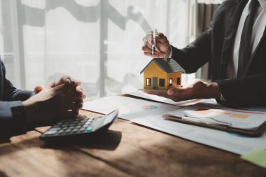 Bir emlak uzmanıyla, emlak yatırımlarıyla ilgili görüşmeler yapan bir müşteri, bir yatırım uzmanıyla gayrimenkul satın alımıyla ilgili finansal bir toplantı yapıyor..