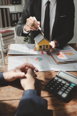 Bir emlak uzmanıyla, emlak yatırımlarıyla ilgili görüşmeler yapan bir müşteri, bir yatırım uzmanıyla gayrimenkul satın alımıyla ilgili finansal bir toplantı yapıyor..