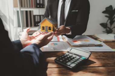 Bir emlak uzmanıyla, emlak yatırımlarıyla ilgili görüşmeler yapan bir müşteri, bir yatırım uzmanıyla gayrimenkul satın alımıyla ilgili finansal bir toplantı yapıyor..