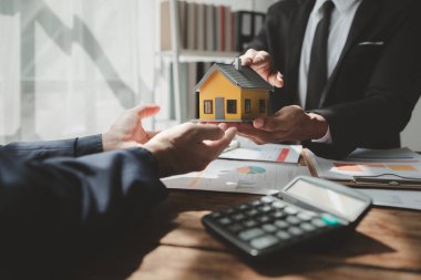 Bir emlak uzmanıyla, emlak yatırımlarıyla ilgili görüşmeler yapan bir müşteri, bir yatırım uzmanıyla gayrimenkul satın alımıyla ilgili finansal bir toplantı yapıyor..