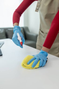 Ofisteki masa yüzeyini dezenfektan spreyiyle temizlemek, eldiven giymek ve masayı havluyla silmek, temizlikçi, temizlik için çalışma masasını temizliyor çünkü Covid-19, temizlik fikri....