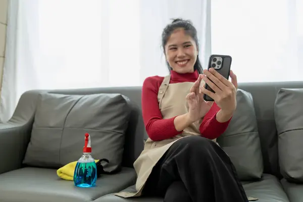 The housekeeper is relaxing after cleaning the house, Playing on the phone on the sofa, Watch videos on your smartphone after cleaning the house, relaxing idea.