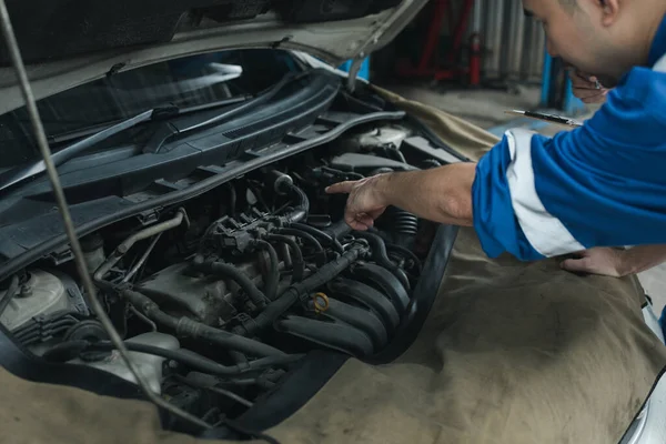 The mechanic is repairing the engine, A car repair worker is inspecting a car, A car mechanic is looking at what is the problem with the engine in the garage.
