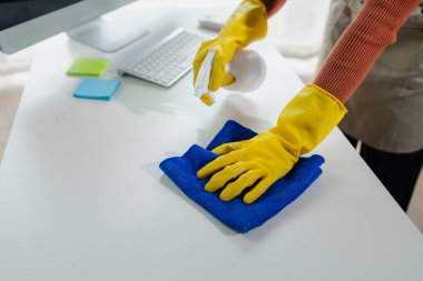 Ofisteki masa yüzeyini dezenfektan spreyiyle temizlemek, eldiven giymek ve masayı havluyla silmek, temizlikçi, temizlik için çalışma masasını temizliyor çünkü Covid-19, temizlik fikri....