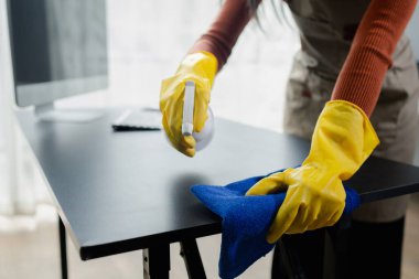 Cleaning desk surface in office with sanitizer spray, wear gloves and wipe the table with a towel, the housekeeper is cleaning the work desk for hygiene because of the Covid-19, cleaning idea. clipart